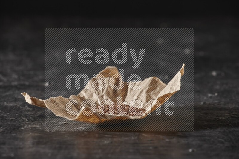 A crumpled piece of paper full of flaxseeds on a textured black flooring