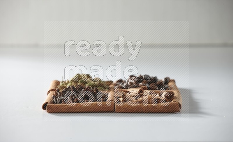 4 مربعات من أعواد القرفة ممتلئة بحبوب القهوة والقرفة والقرنفل والهيل على أرضية بيضاء