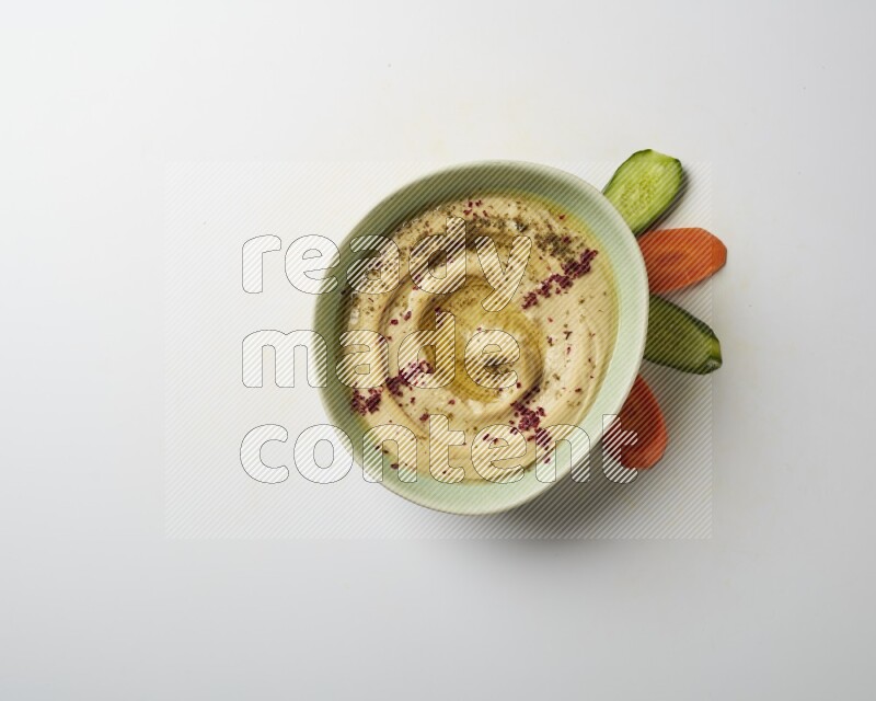 Hummus in a green plate garnished with zattar & sumak on a white background