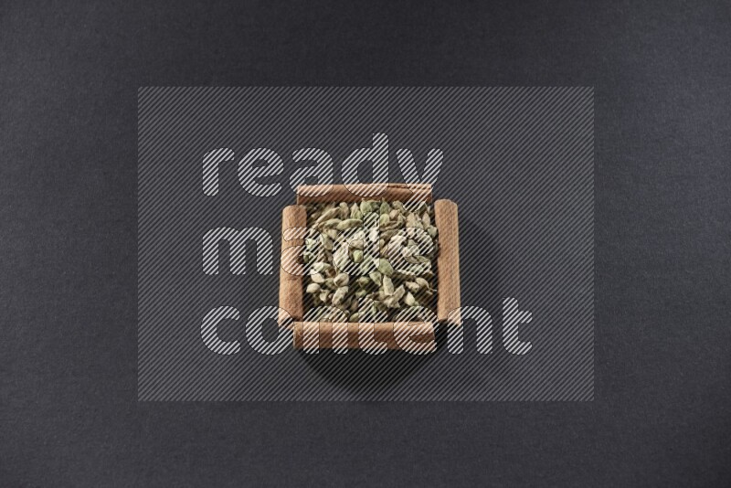 أربعة من أعواد القرفة مكونة شكل مربع بداخلها حبوب الهيل علي خلفية سوداء