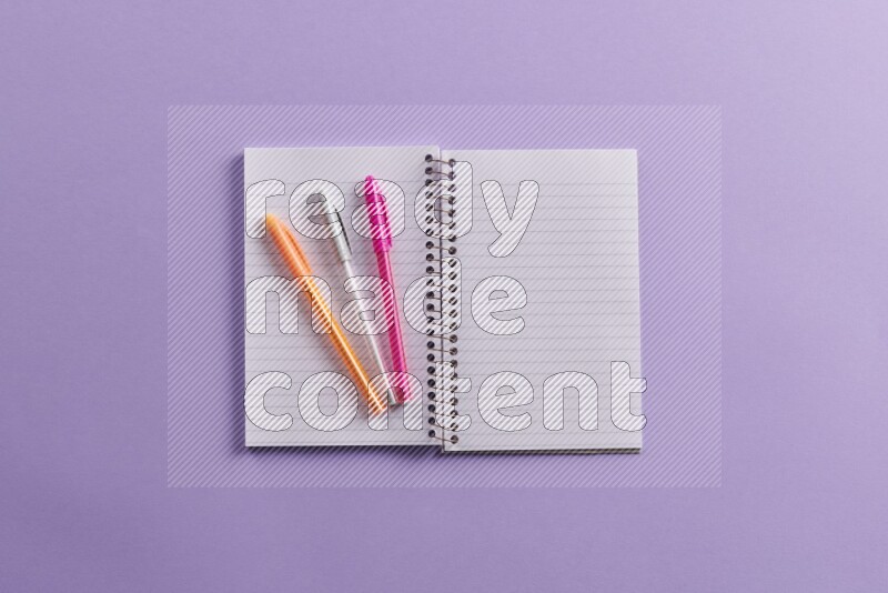 A blank open notebook with school supplies on purple background