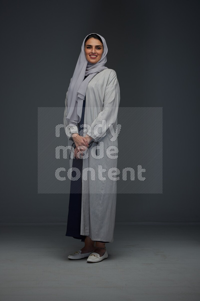 A Saudi woman wearing a light gray Abaya and head scarf standing and making multi poses eye level on a grey background