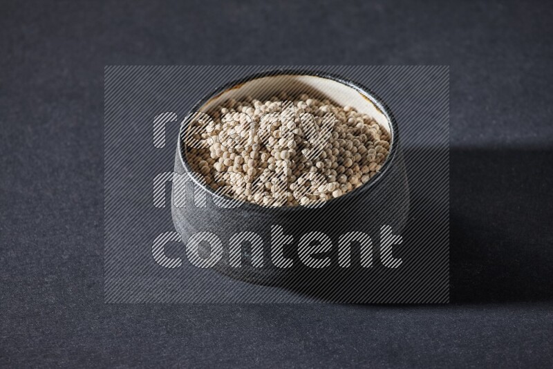 وعاء فخار أسود مملوء بالفلفل الأبيض على أرضية سوداء
