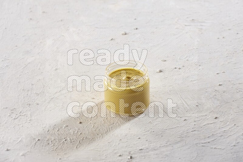 A glass jar full of mustard paste on a textured white flooring
