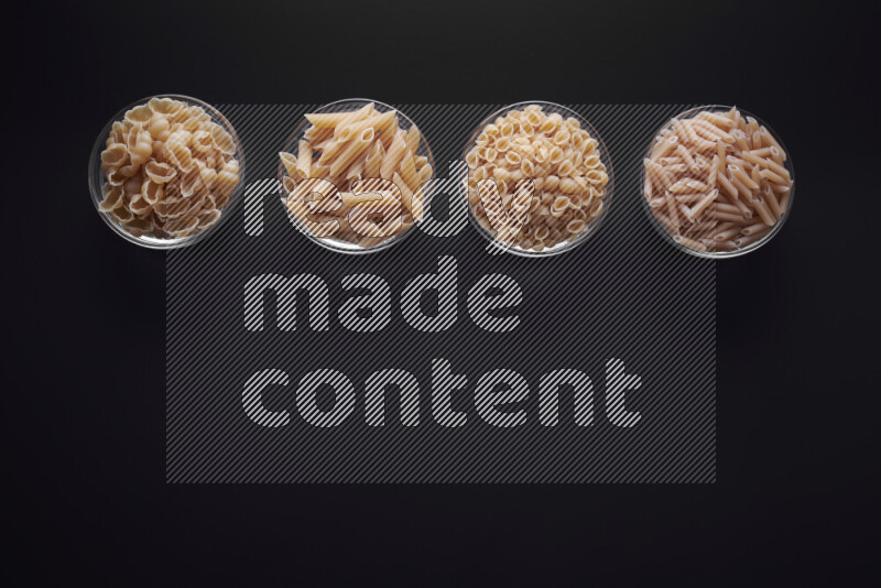 Different pasta types in glass bowls on black background