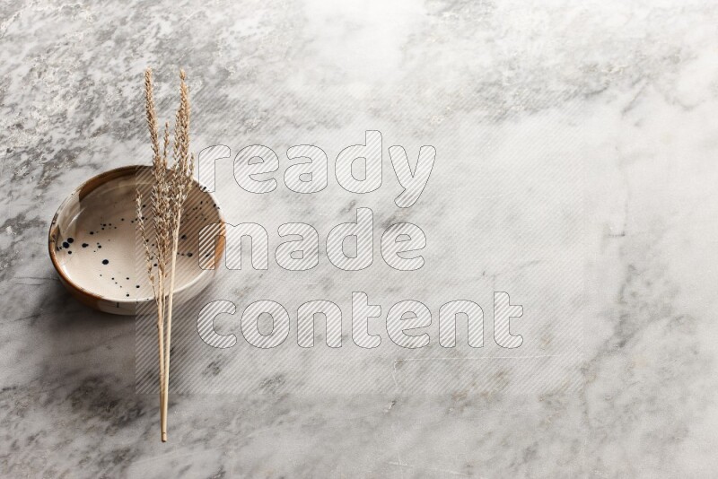 Wheat stalks on multicolored pottery bowl on grey marble background