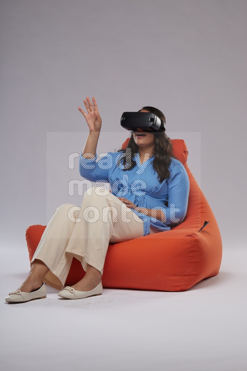 A woman sitting on an orange beanbag and gaming with VR
