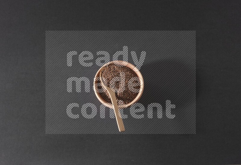 وعاء خشبي ممتلئ بحبوب بذر الكتان مع ملعقة خشبية ممتلئة بالحبوب علي خلفية سوداء