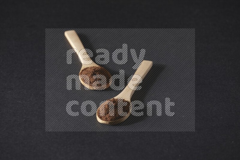 ملعقتان خشبيتان ممتلئتان ببودرة القرنفل على خلفية سوداء