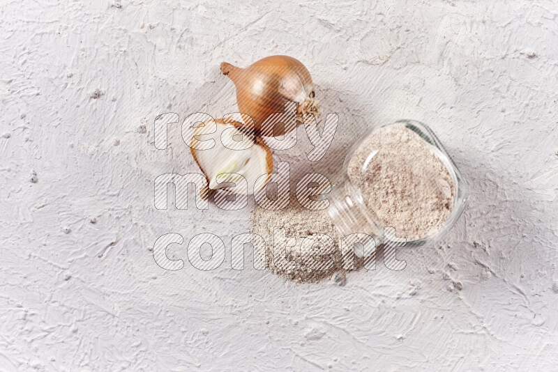 A glass jar full of onion powder flipped with some spilling powder on white background