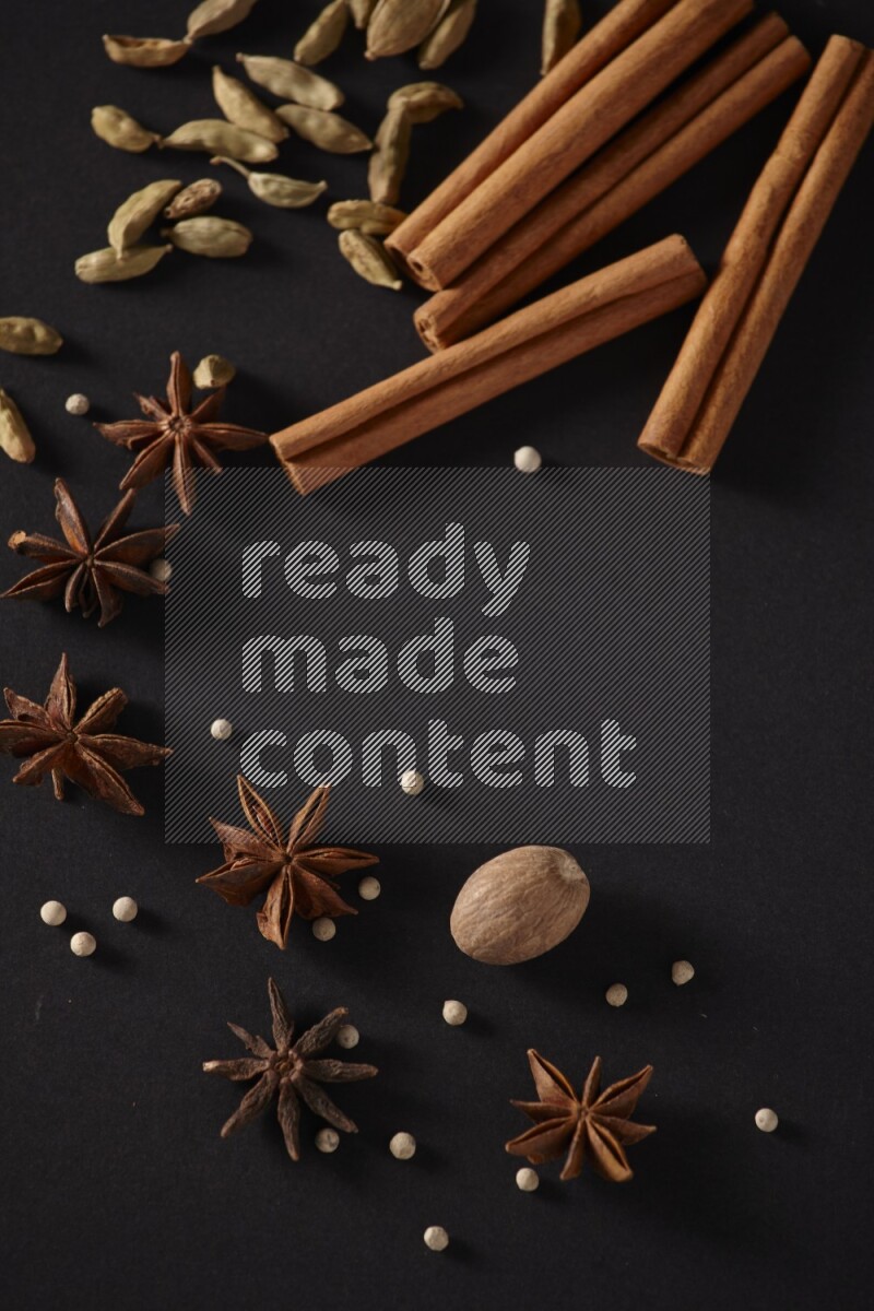 أعواد من القرفة وحبوب الهيل واليانسون النجمي وجوزة الطيب وحبوب الفلفل الأبيض علي خلفية سوداء