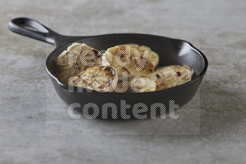 half's roasted garlic in a black pan on a grey textured countertop