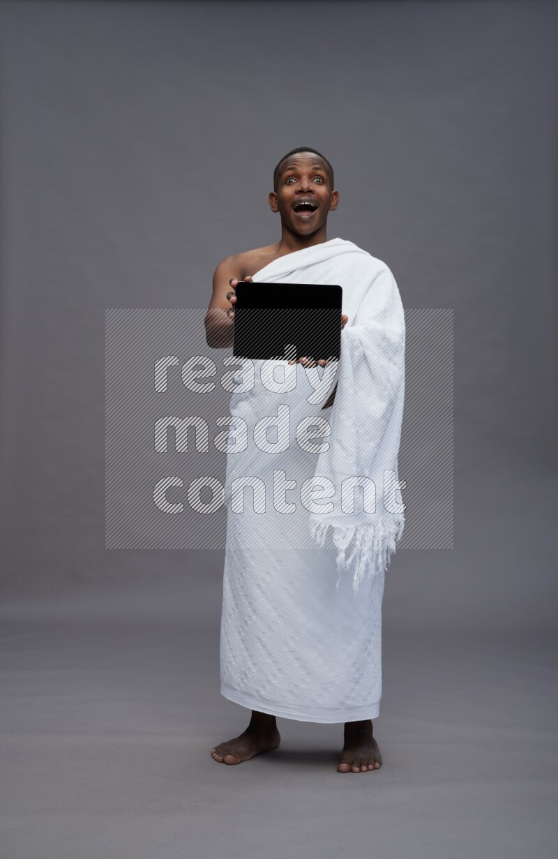 A man wearing Ehram Standing showing tablet to camera on gray background