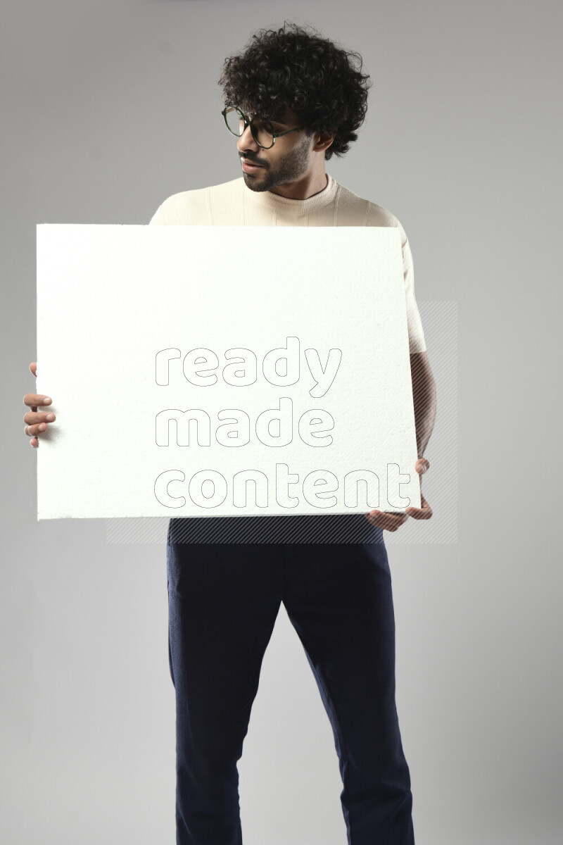 رجل يرتدي ملابس كاجوال يحمل لوحة بيضاء علي خلفية بيضاء