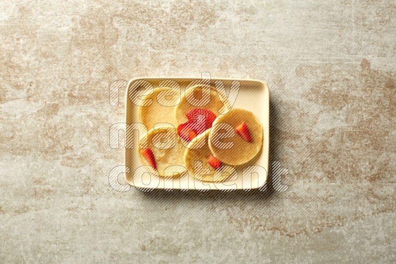 Five stacked strawberry mini pancakes in a rectangular plate on beige background