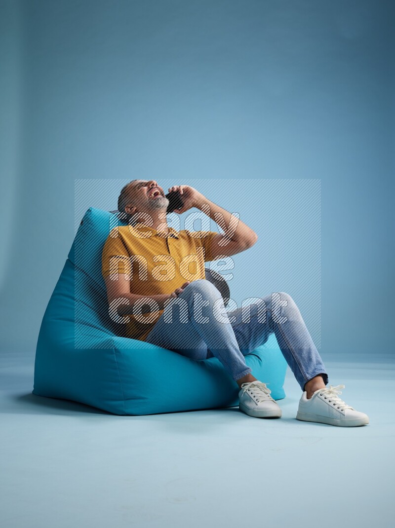 A man sitting on a blue beanbag and talking on the phone