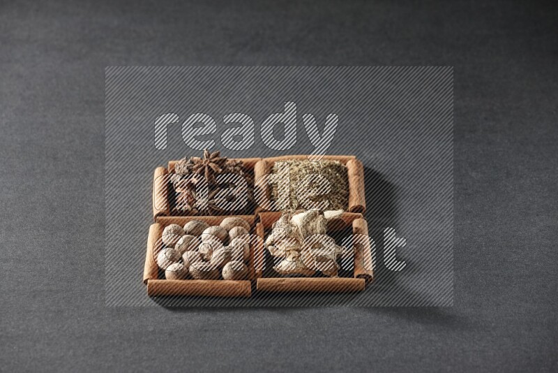 4 مربعات من عيدان القرفة ممتلئة باليانسون النجمي والكمون والزنجبيل المجفف وجوزة الطيب على أرضية سوداء