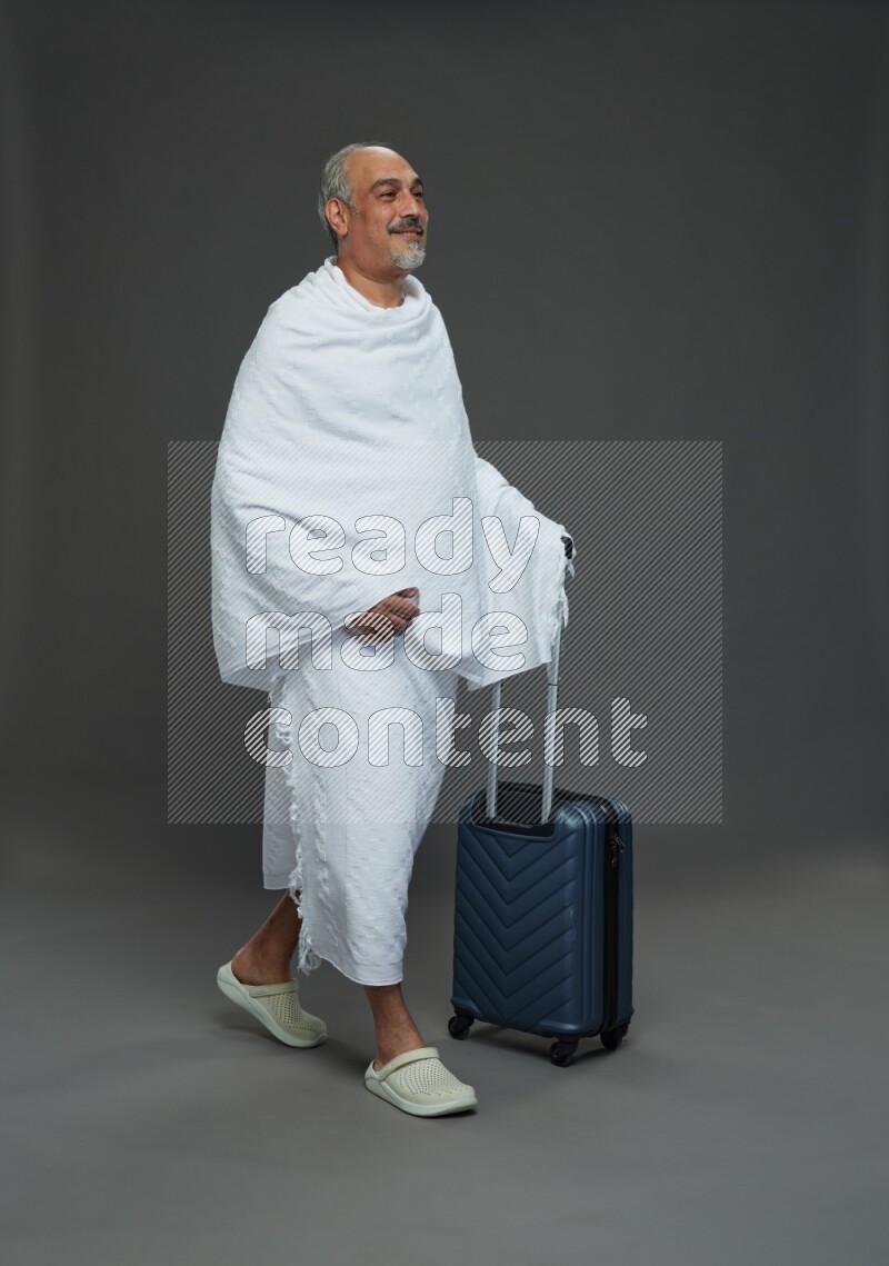 A man wearing Ehram Standing holding traveling bag on gray background