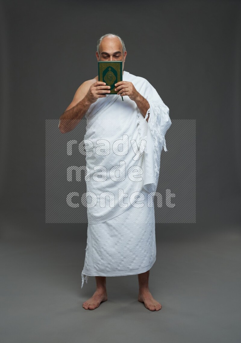 A man wearing Ehram Standing reading quran on gray background