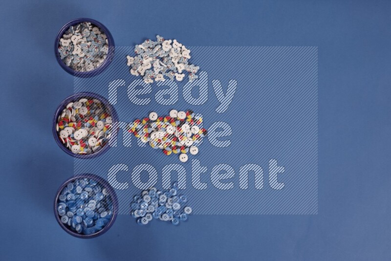 Multicolored pottery bowls full of colored buttons on blue background