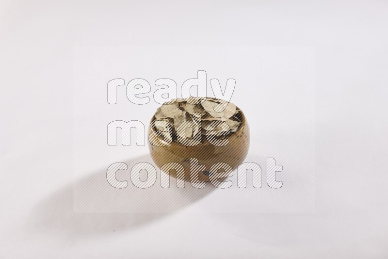 A multicolored pottery bowl full of dried bay leaves on white flooring in different angles