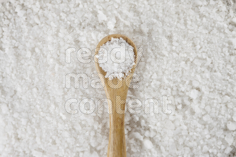 A wooden spoon full of white salt on white background