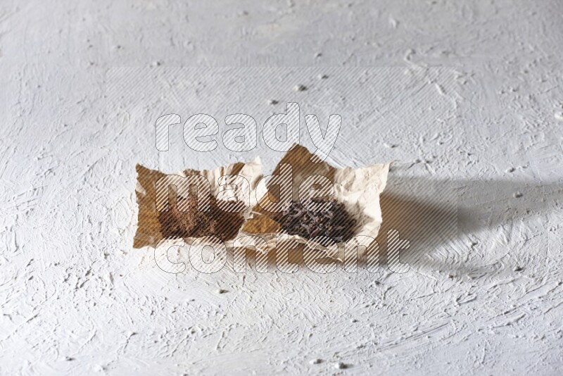 Cloves powder and cloves on 2 crumpled pieces of paper on a textured white flooring