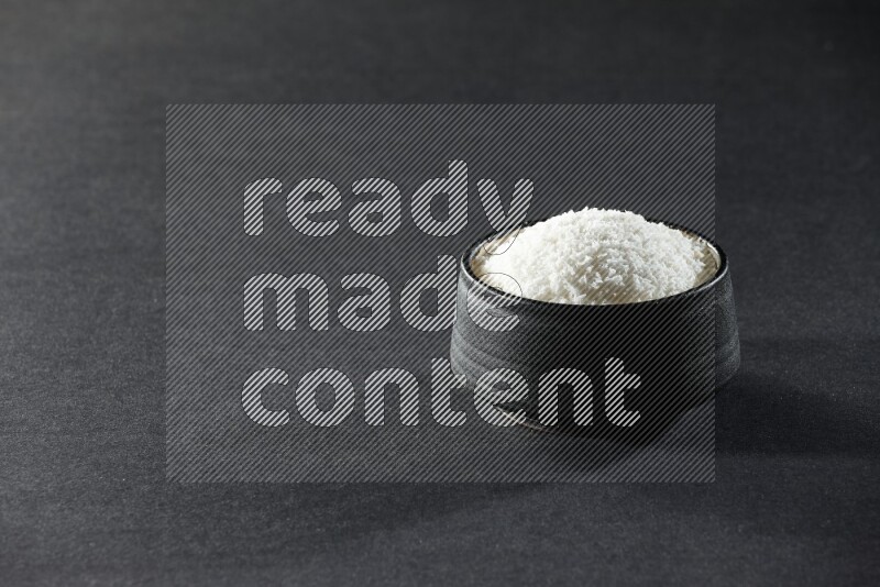 A black pottery bowl full of desiccated coconut on a black background in different angles