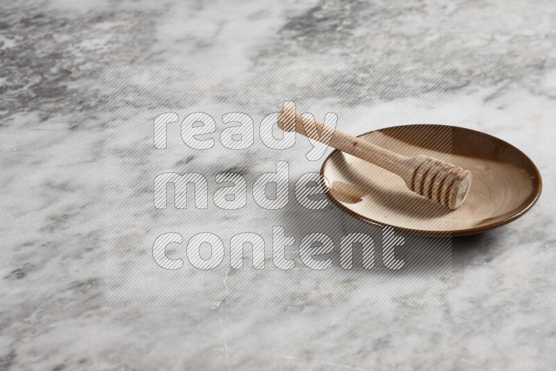 Multicolored pottery plate with wooden honey dipper in it on grey marble background