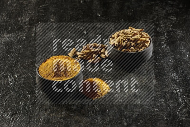 وعاءان من الفخار باللون الأسود، أحدهما ممتلئ ببودرة الكركم والآخر ممتلئ بأصابع كاملة من الكركم المجفف على خلفية سوداء