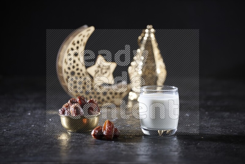 Dates in a metal bowl with milk beside golden lanterns in a dark setup