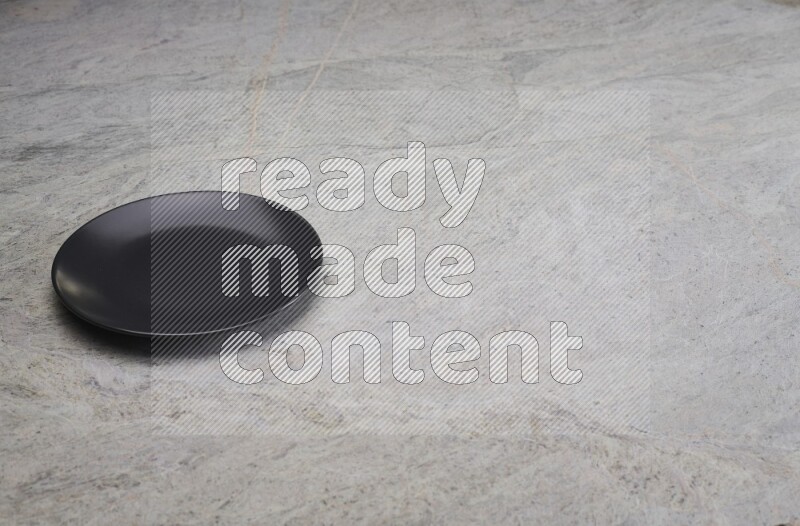 A black ceramic circular plate on grey marble background