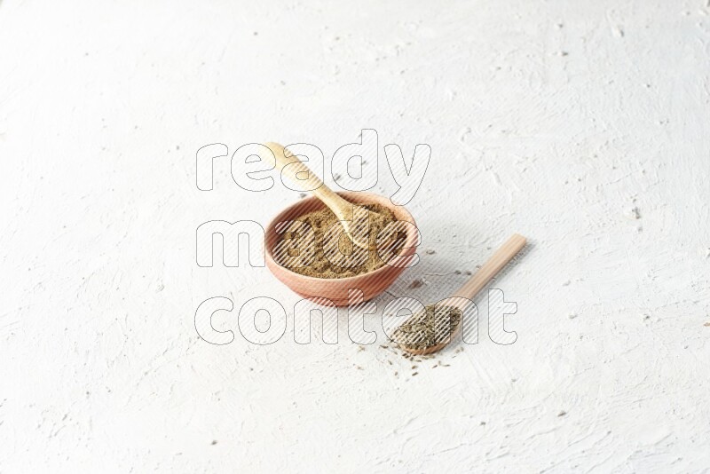 A wooden bowl and 2 wooden spoons full of cumin powder and cumin seeds on textured white flooring