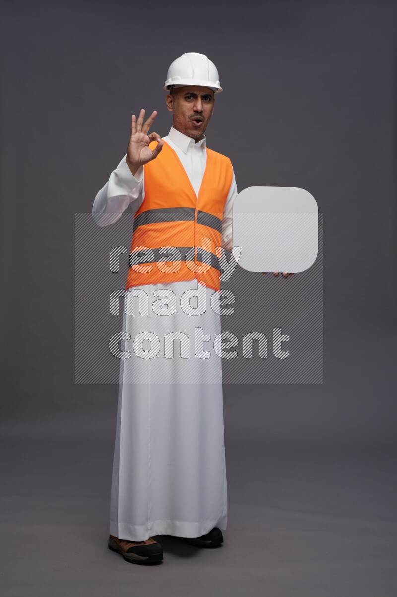 Saudi man wearing thob with engineer vest standing holding social media sign on gray background