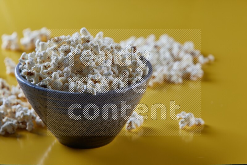 A multicolored pottery bowl full of popcorn with popcorn beside it on a yellow background in different angles