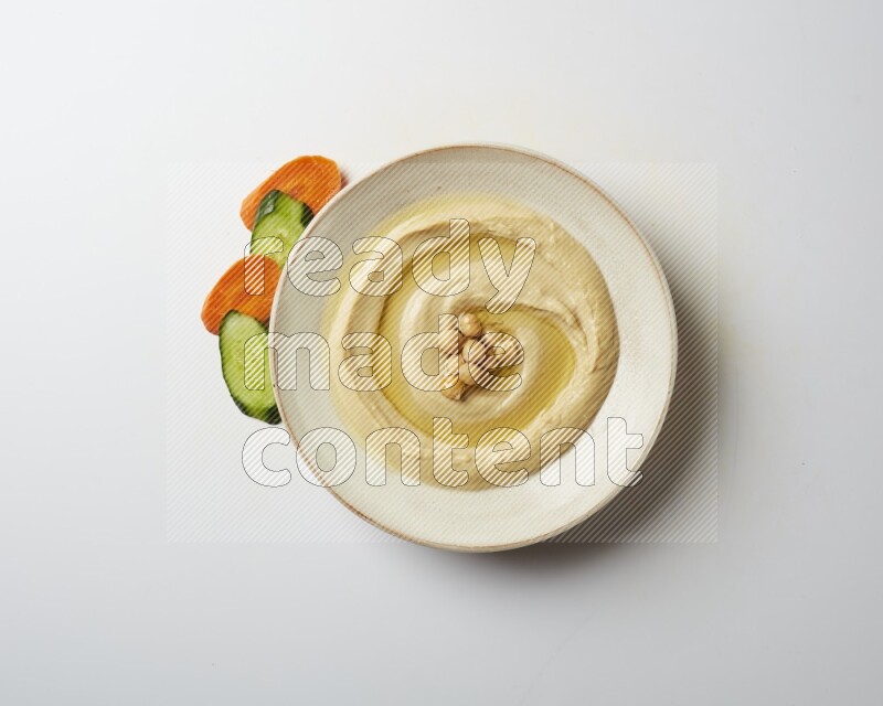 Hummus in a pottry plate garnished with roasted chickpeas on a white background