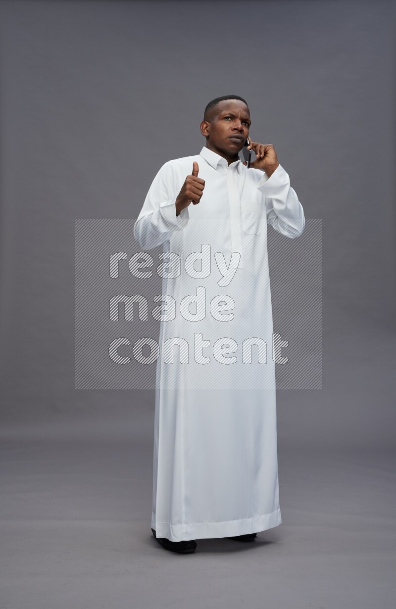 Saudi man wearing thob standing talking on phone on gray background