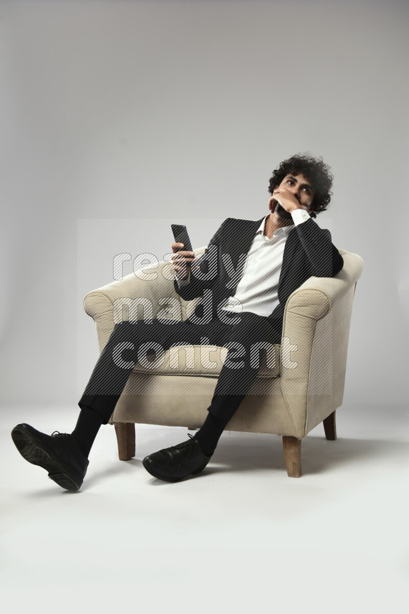 A man wearing formal sitting on a chair texting on the phone on white background