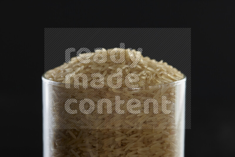 Basmati golden rice in a glass jar on black background