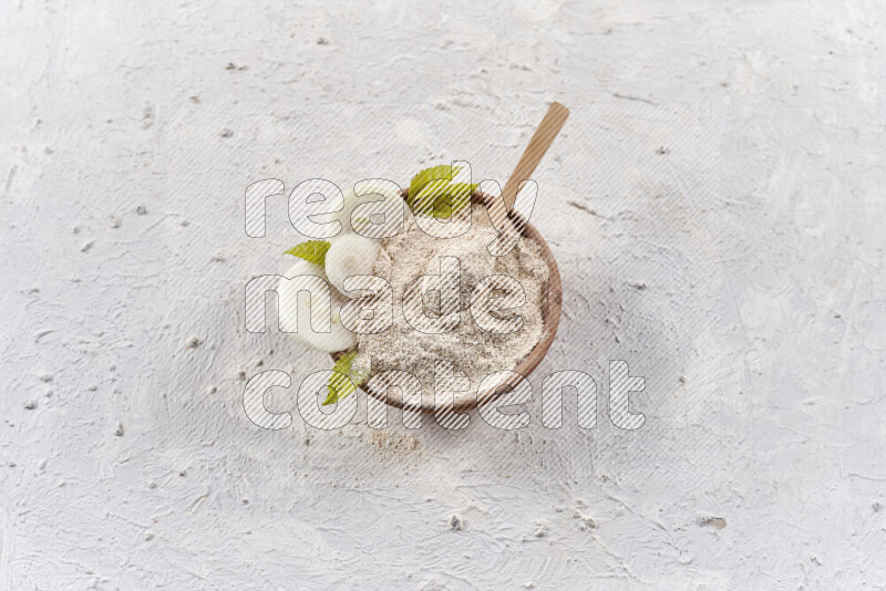 A wooden bowl full of onion powder with a wooden spoon in it with some sliced onions on white background