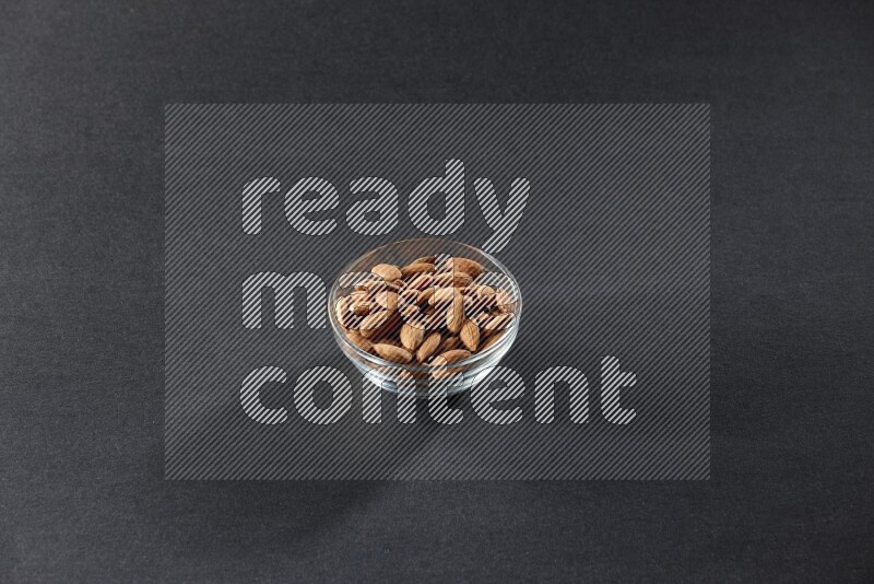 A glass bowl full of peeled almonds on a black background in different angles