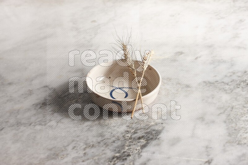 Wheat stalks on multicolored pottery bowl on grey marble background