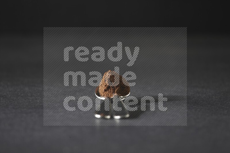 2 metal spoons on top of each other full of cloves powder on a black flooring