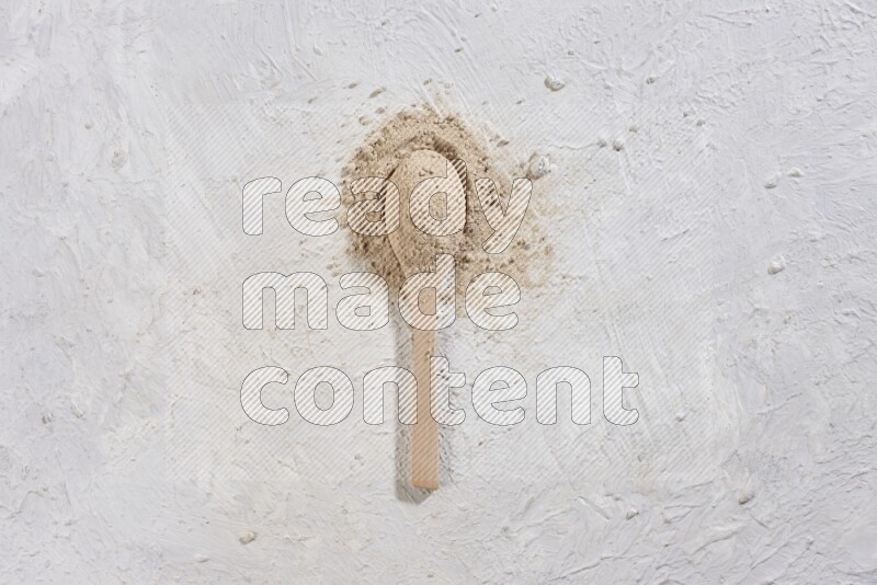 A wooden spoon full of garlic powder with scattered powder around it on a textured white flooring