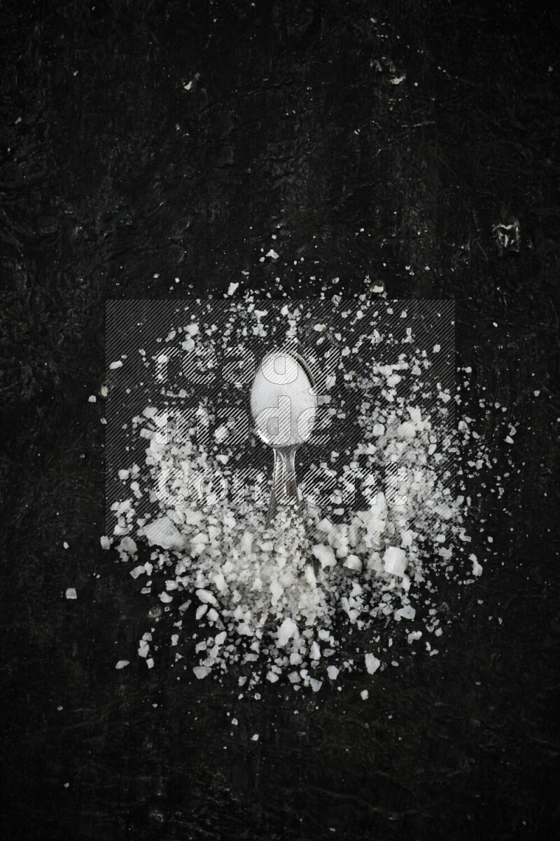 2 metal spoons filled with white salt on black background