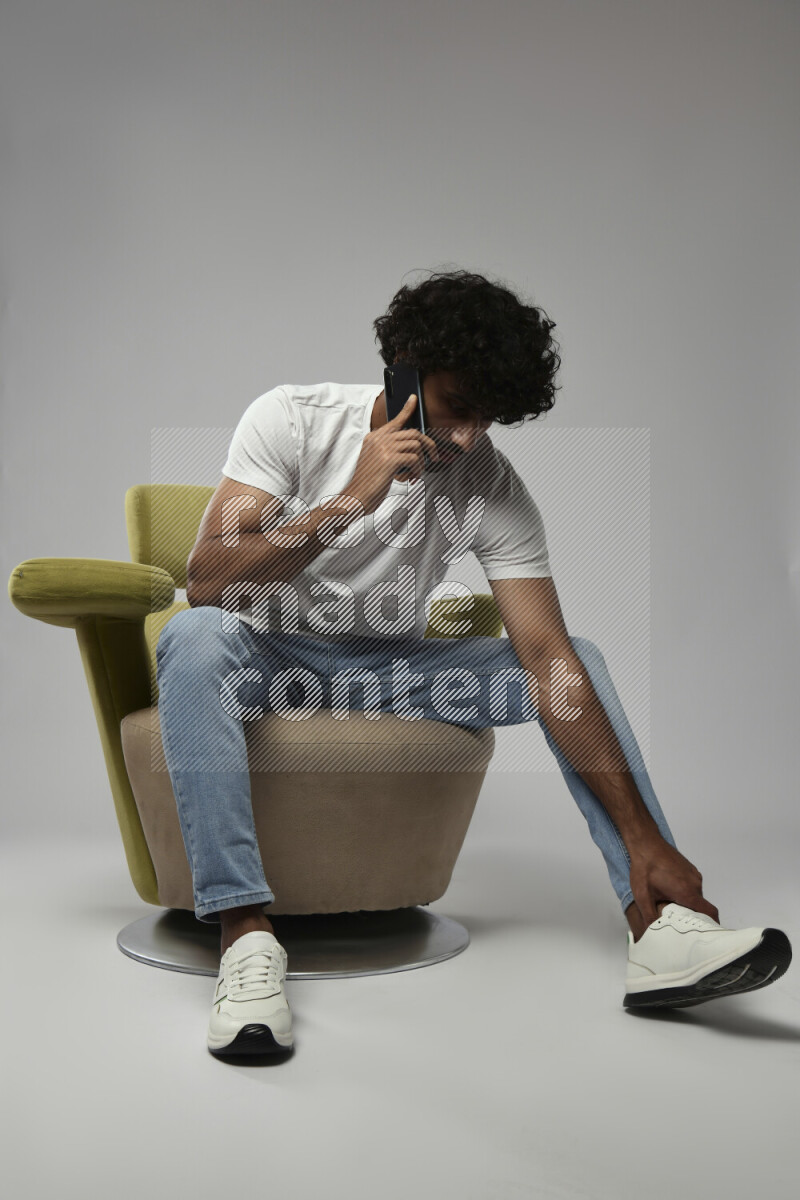 A man wearing casual sitting on a chair talking on the phone on white background