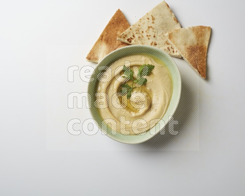Hummus in a green plate garnished with parsley on a white background
