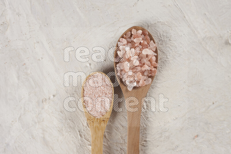 2 wooden spoons filled with fine and coarse salt on white background