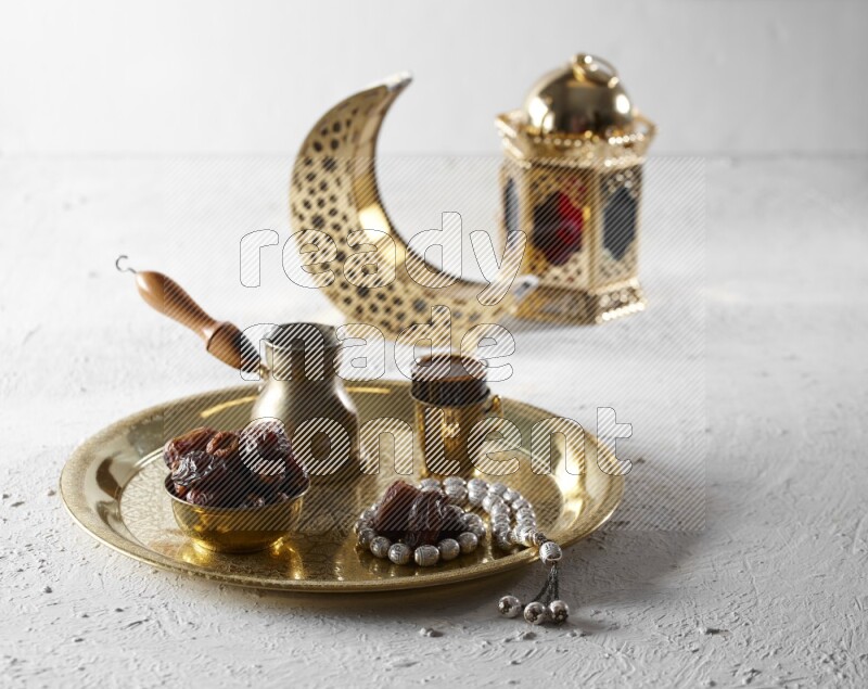 Dates in a metal bowl with coffee and prayer beads on a tray beside lanterns in a light setup