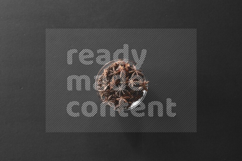 A glass bowl full of star anise on black flooring